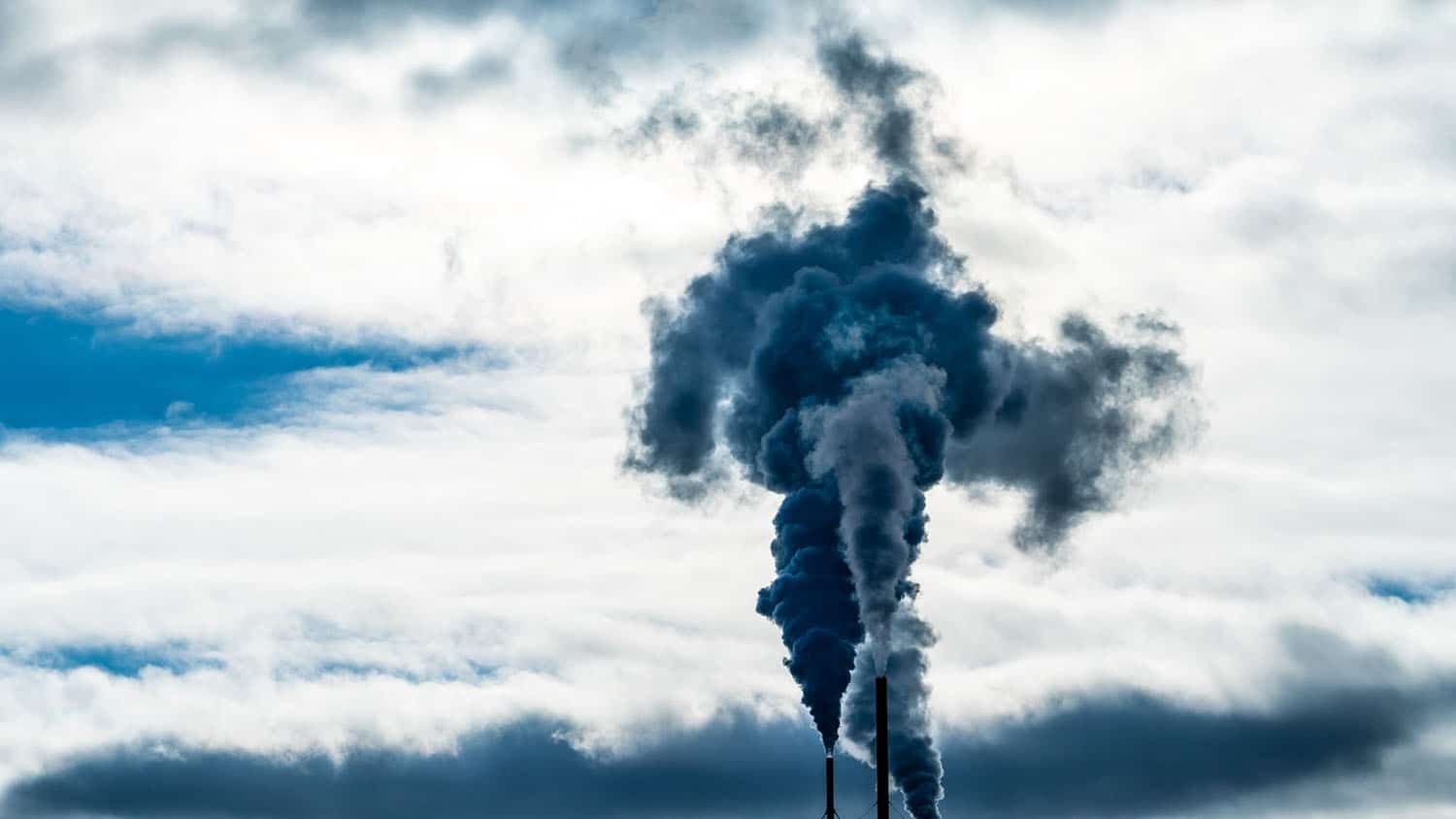 smoke stacks spew opaque gases into the blue sky